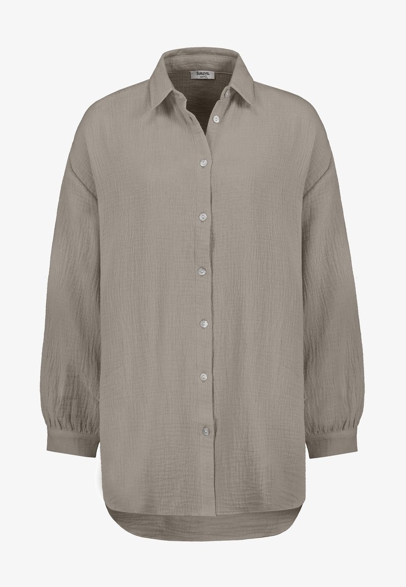 Long-sleeve, button-up shirt in light taupe, featuring a textured fabric, a classic collar, and a curved hemline with slight gathers at the cuffs.