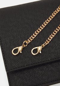 Schwarze, strukturierte Handtasche mit einem goldenen Kettenriemen und Karabinerhakenverschluss, detaillierter Nahtführung und einem eleganten Design.