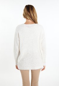 Maglione bianco e soffice con una vestibilità ampia, colletto rotondo e superficie testurizzata. Si ferma vicino ai fianchi con un retro leggermente più lungo. Abbinato a pantaloni beige.