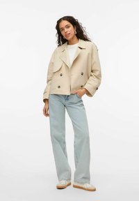 Beež kahe nööpauguga trench coat suure kraega ja nööbiga detailidega, koos helesiniste laiemate pükstega ja mugavate tossudega.