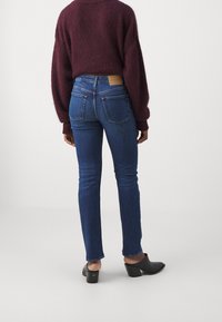 Smala jeans i mörk tvättad denim, hög midja med bakfickor; kombinerade med en bordeauxfärgad tröja och svarta klackmules.