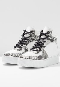 Höga sneakers med en vit läderkropp och pythonmönstrade detaljer. Har svarta snörningar och en strukturerad vit gummisula.
