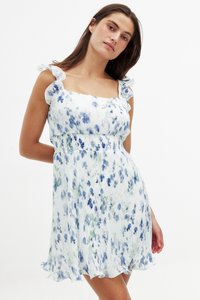 Robe florale avec des motifs bleus et verts sur fond blanc. Elle présente des bretelles volantées et un ourlet en couches. Fabriquée en tissu léger.