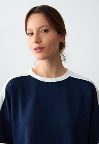 Marineblauwe sweatshirt met witte accenten. Heeft een ronde hals en korte mouwen. Glad van structuur en een ontspannen pasvorm. Eenvoudig, modern ontwerp.