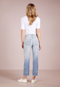 Vybledlé světle modré džíny s distressed designem, surovými lemy a dvěma zadními kapsami, spárované s bílou přiléhavou košilí a bílými teniskami.