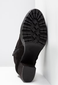 Botín negro de ante con suela de goma texturizada, que muestra un tacón bajo y un detalle de cremallera lateral.