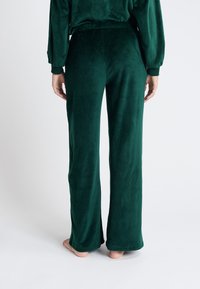 Groene velours wijde pijpen met een gladde textuur, voorzien van een elastische tailleband en een relaxte pasvorm, gezien vanuit de achterkant.