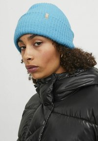 Jasnoniebieska, dziergana czapka z ryżowym splotem, w połączeniu z czarną, błyszczącą kurtką puchową zapinan�ą na napy z wysokim kołnierzem.