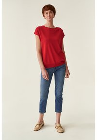Suéter rojo de manga corta con un ajuste relajado, combinado con jeans cortos de color azul claro y mocasines beiges con detalles de herrajes dorados.