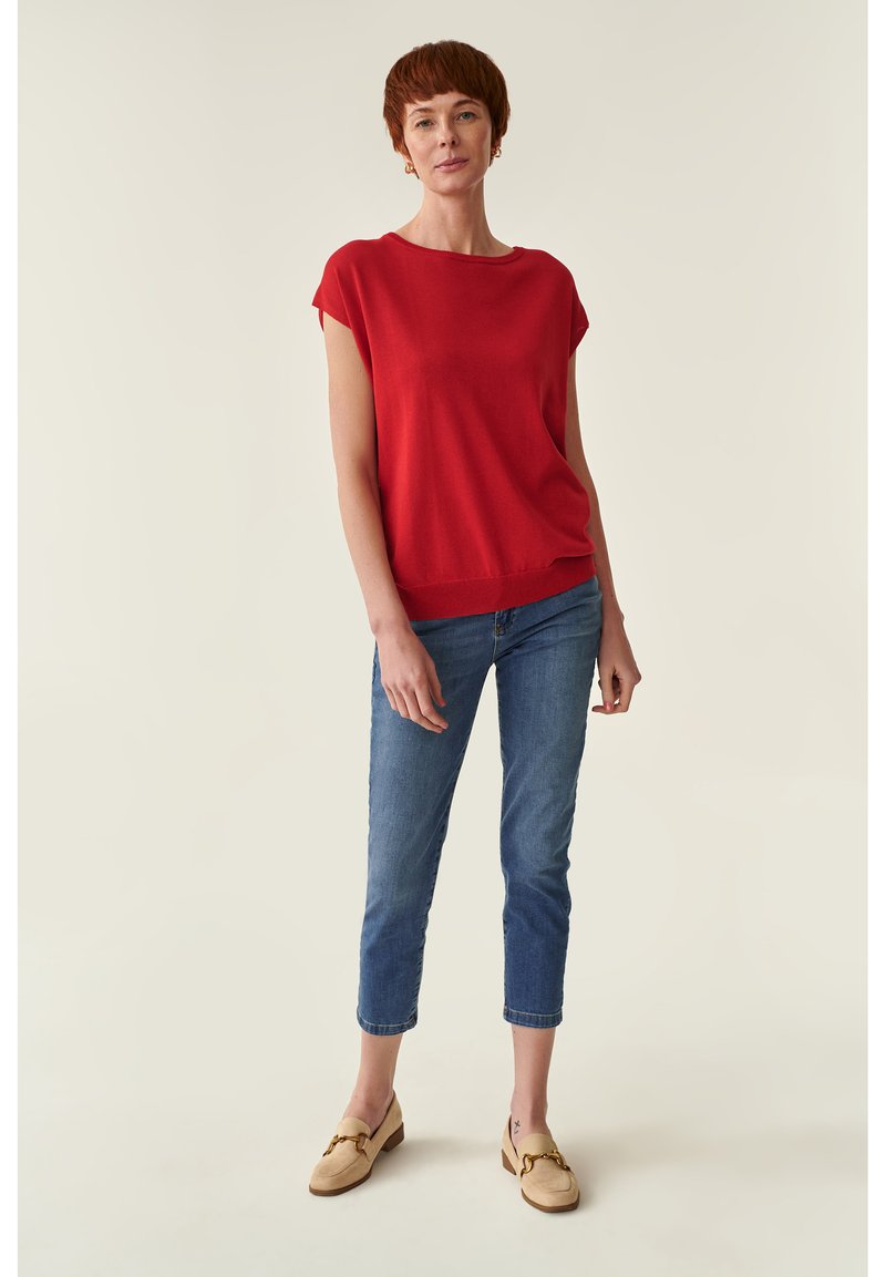 Suéter rojo de manga corta con un ajuste relajado, combinado con jeans cortos de color azul claro y mocasines beiges con detalles de herrajes dorados.