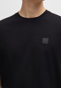 Svart bomullströja med rundad halsringning, prydd med en fyrkantig svart tygpatch med "BOSS" präglat i mitten på bröstet.