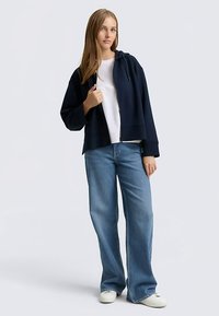 Marineblauwe cropped hoodie met een ritssluiting aan de voorkant, gecombineerd met lichtgewassen jeans met brede pijpen en witte sneakers. Glad materiaal, losse pasvorm.