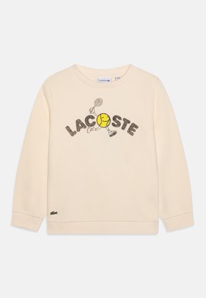 Sweatshirt couleur crème avec le texte "LACOSTE" et un graphique amusant de balle de tennis. Poignets et ourlet côtelés, avec un petit logo en bas à gauche.