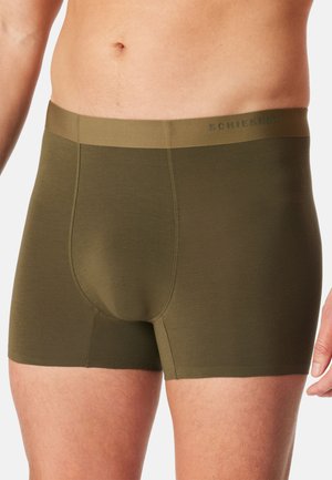 Männlicher Oberkörper, der olivgrüne Boxershorts mit einem passenden Bund trägt, der auf der rechten Seite ein dezentes Markenlogo aufweist.