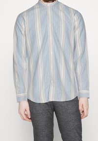 Overhemd in lichtblauw met verticale strepen in verschillende breedtes, gemaakt van een lichtgewicht stof. Voorzien van een mandarin kraag en lange mouwen.