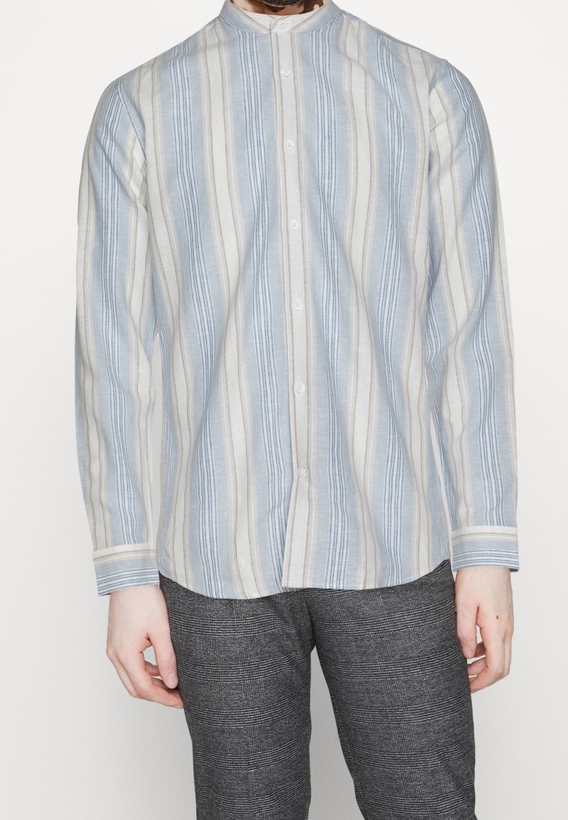 Overhemd in lichtblauw met verticale strepen in verschillende breedtes, gemaakt van een lichtgewicht stof. Voorzien van een mandarin kraag en lange mouwen.