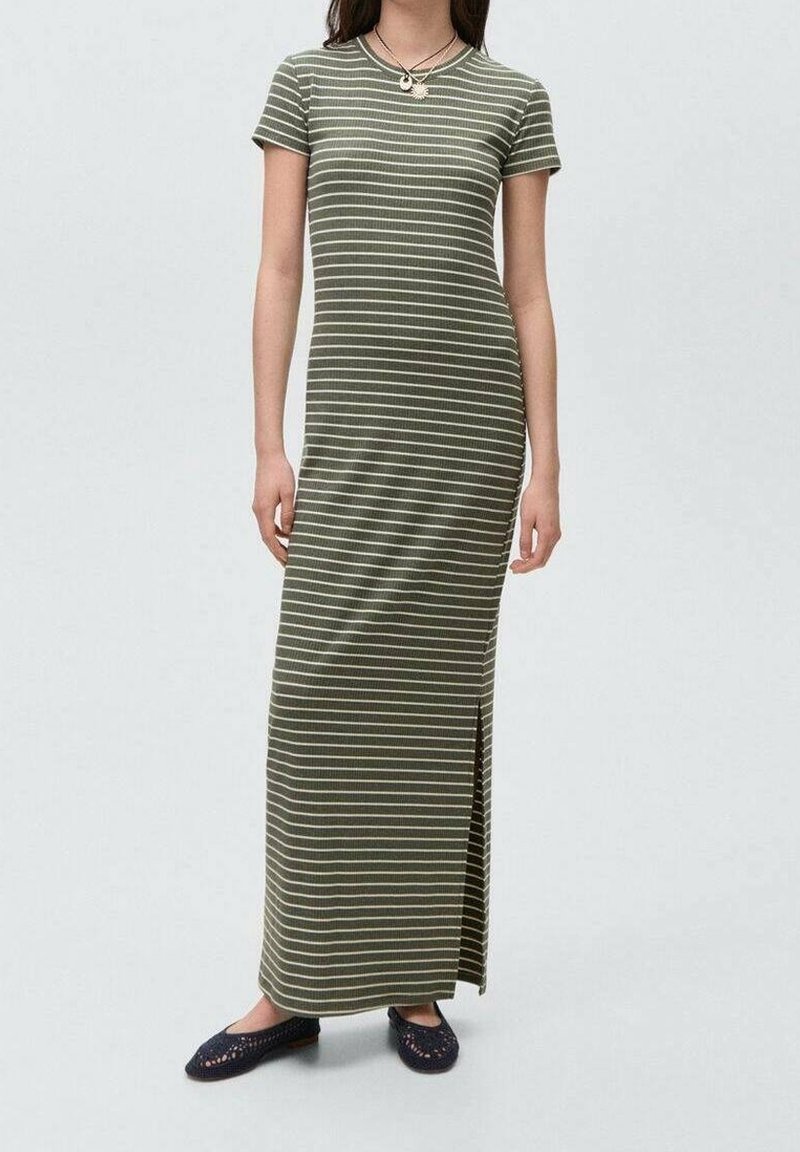 Femme portant une robe maxi à manches courtes rayée vert olive et blanc avec une fente latérale et des chaussures noires slip-on.