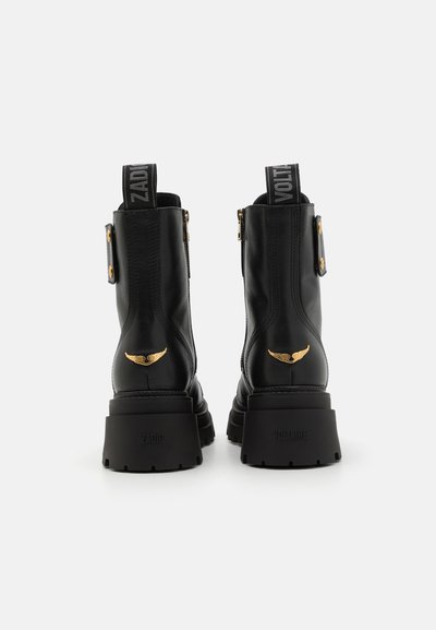 Svarta läderankelboots med kraftiga sulor, guldaccenter och märkesdragöglor. Utrustad med två sidogespar och präglade logotyper på klackarna.