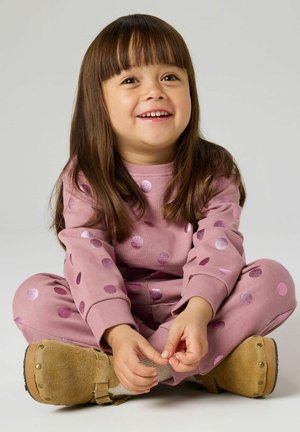 Lyserødt pyjamasæt med skinnende prikker, lange ærmer og elastiske manchetter; kombineret med beige slip-on sko med metalaccenter.