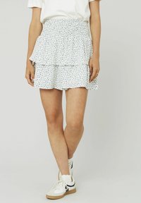 Jupe blanche à volants avec motif floral bleu, taille smockée, tissu léger et ourlet festonné. Associée à des baskets décontractées.
