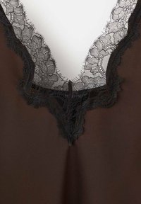 Bruine stof met een diepe V-hals. Zwarte kanten afwerking langs de halslijn met bloemmotieven, die een gestructureerd detail toevoegen.