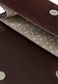 Brązowa skórzana torebka z miękkim zwiewnym klapem, z metalowym zatrzaskiem w kolorze srebrnym oraz wzorzystą podszewką w jaśniejszym odcieniu.
