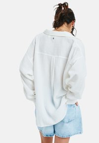 Witte ontspannen fit shirt met een gestructureerde stof, kraag en verlengde schouders. Gecombineerd met lichtblauwe denim shorts en zichtbare achternaad details.