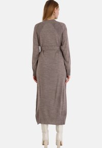 Pitkä neulottu mekko hillityssä ruskeassa sävyssä, jossa on ribbipinta ja istuva vyö. Hihat ja helma ovat hieman ribbattuja.
