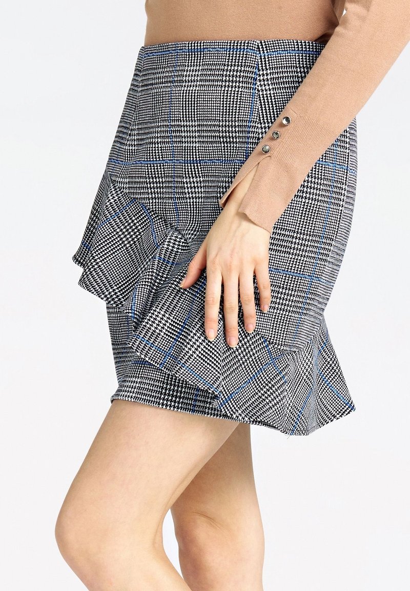 Jupe à carreaux noir et blanc avec des accents bleus, ourlet évasé et détail à volants. Fabriquée en tissu texturé, avec une taille ajustée.