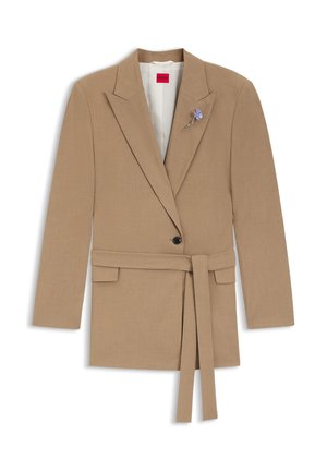 Béžové sako na mieru s opaskom, výrezom na klopách, zapínaním na jeden gombík a fialovou kvetinovou brošňou na hrudi. Hladká textúra látky.