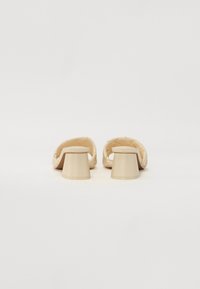Beige woven slide sandals with a textured upper, rounded toe, and narrow heels; a smooth, glossy finish on the platform.