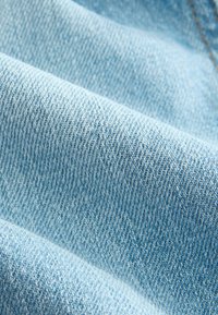 Gros plan de la texture d’un tissu en denim bleu clair montrant des fils tissés et des plis subtils.