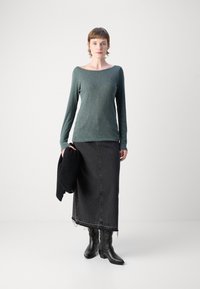 Ilga rankovė, tamsiai žalia lino palaidinė, derinama su juoda džinsine maksi sijonu, kuriame yra suplėšytos kraštai, ir juodais aulinukais. Laiko juodą megztinį.