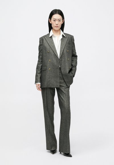 Sivi prugasti dvoredni odijelo s strukturiranim sakoom i hlačama ravnog kroja, uparenim s bijelom košuljom s ovratnikom.