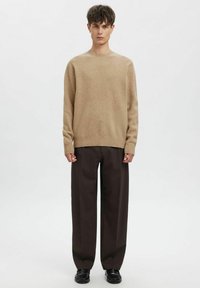 Beżowy wełniany sweter z okrągłym dekoltem, zestawiony z ciemnobrązowymi szerokimi spodniami i czarnymi butami. Prosty, fakturowany wzór dzianiny.