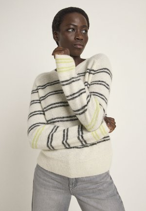 Cremfarbener Pullover mit schwarzen und grünen Streifen, aus weichem Material. Verfügt über eine lockere Passform und gerippte Bündchen, kombiniert mit hellgrauen Jeans.