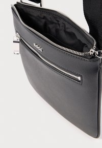 Μαύρη συνθετική τσάντα ώμου με υφή, διαθέτει κύριο διαμέρισμα με φερμουάρ και μπροστινή τσέπη με φερμουάρ, καθώς και ασημένιες μεταλλικές λεπτομέρειες.