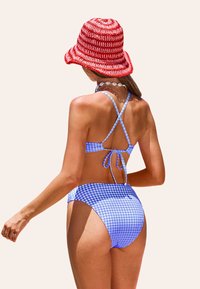 Bikini de cuadro vichy azul y blanco con tirantes cruzados y cierre de lazo, combinado con un sombrero de cubo a rayas rojas y blancas.