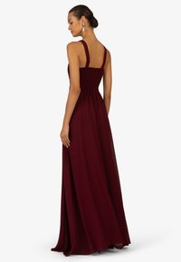 Bordeaux maxi-jurk met dikke bandjes, gerimpelde buste en vloeiende rok. Gemaakt van lichte stof, met een gladde textuur en volle lengte.