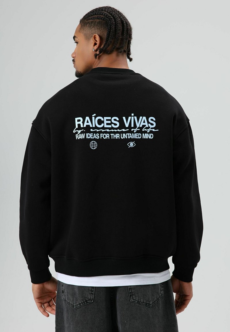 Sweat-shirt noir à coupe décontractée, avec un texte bleu au dos : "RAÍCES VIVAS" et d'autres éléments graphiques en dessous. Matière en coton.