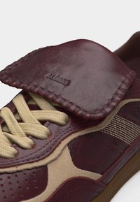 Κοντινό πλάνο μαρουνί και μπεζ αθλητικού παπουτσιού με μπεζ κορδόνια, υφασμένο δερμάτινο καπάκι με ανάγλυφο το λογότυπο "Alohas" και λεπτομερή ραφή στις άκρες της σόλας.