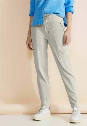 Pantaloni jogger grigio chiaro con un cinturino regolabile in vita, tasche laterali e una texture liscia, abbinati a sneaker bianche e a una maglietta blu.