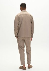 Beige, egyenes szabású blézer, hozzá illő nadrággal párosítva. Puha anyag, mintázat nélkül, és kényelmes slip-on cipő.