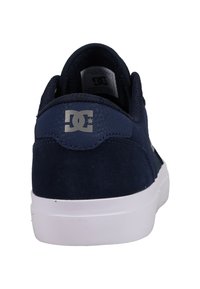 Navy blue sneaker made of suede, featuring a white rubber sole, padded collar, and a silver logo on the back heel.