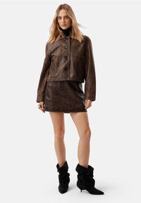 Pruun nahkne lühike jakk ümarate kraega, nööbid ees ning kahe küljetaskuga, koos pruuni kunstnahast mini seeliku ja mustade mahakukkuvate saapatega.