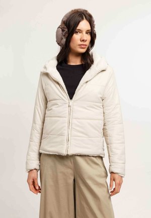 Giacca puffer beige chiaro con cappuccio, dotata di una morbida fodera in pelliccia sintetica e chiusura con zip. Abbinata a pantaloni larghi beige.