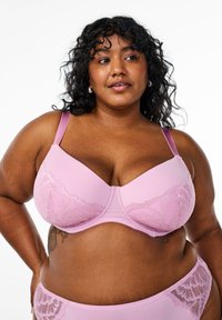 Pink bra with smooth cups, lace detailing at the top, adjustable straps, and a matching pink waistband. Soft texture and supportive design.