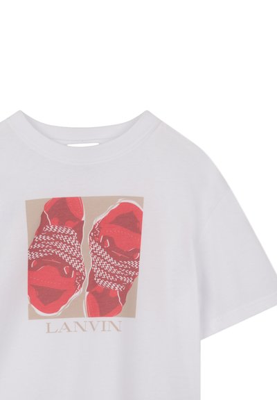 Hvid T-shirt med et grafisk motiv af røde sko med sort-hvide snørebånd på en beige baggrund. "LANVIN" trykt under billedet.