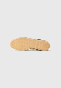 Talpa de pantof din material cauciucat cu un model circular; culoarea este bej deschis cu striații ondulate și un logo în centru.