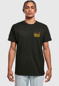 Sort bomulds T-shirt med et farverigt "NEO/MACHI" grafisk design med en kat på venstre bryst. Klassisk pasform med korte ærmer.